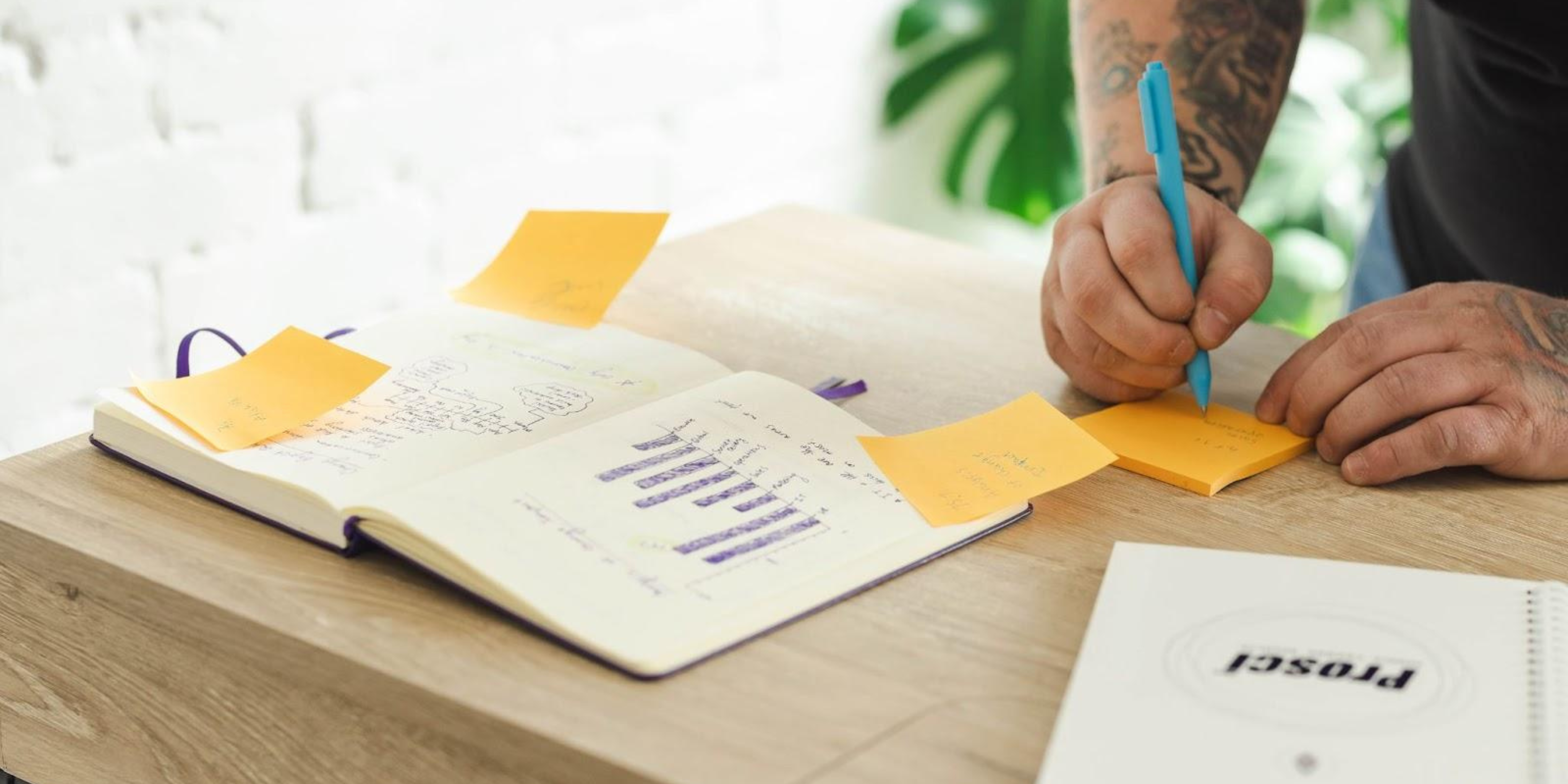 A man ideating notes with two notebooks in the foreground, one labelled 